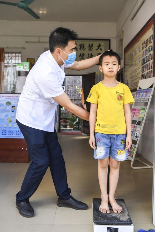 李志辉给村里儿童测量身高体重.