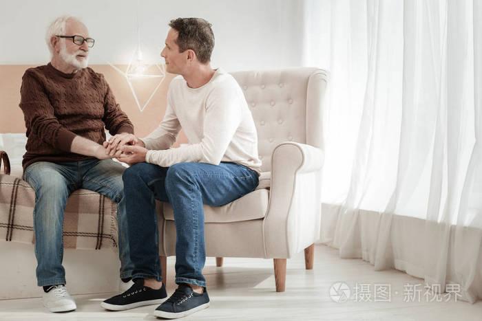 可爱的戴眼镜的父亲坐着看着他的儿子