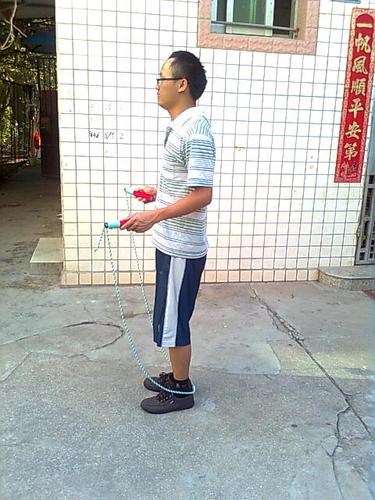 手握跳绳柄,自然弯曲手臂关节置腰两侧呈倒八字状,跳绳至脚后跟后方