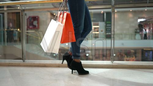 一位女性拿着购物袋和智能手机在商场里走着