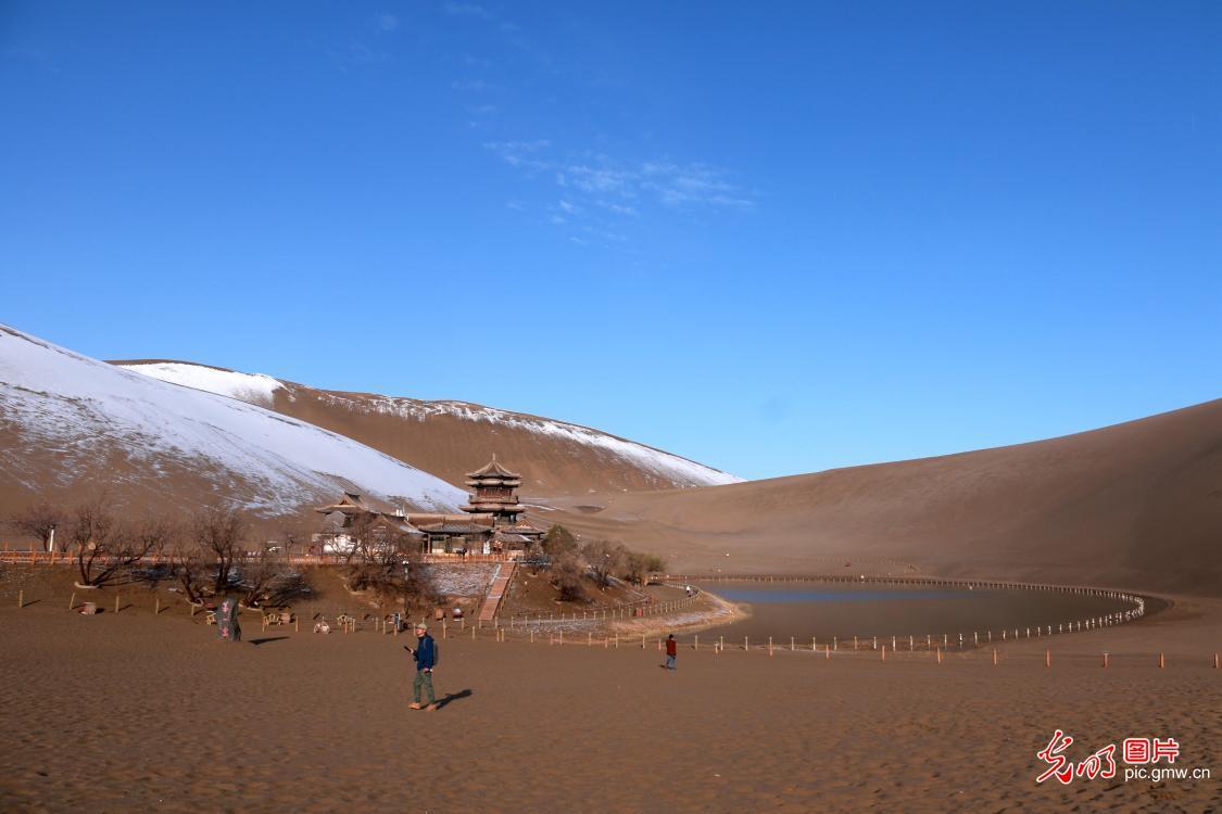 2022年3月25日,游客在甘肃省敦煌市鸣沙山月牙泉景区游览,雪后的月牙