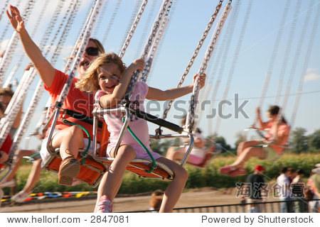 a mother and daughter having fun on amusement park swings.
