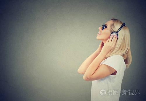 现代女性在休闲t恤和太阳镜中的侧面欣赏耳机中的音乐