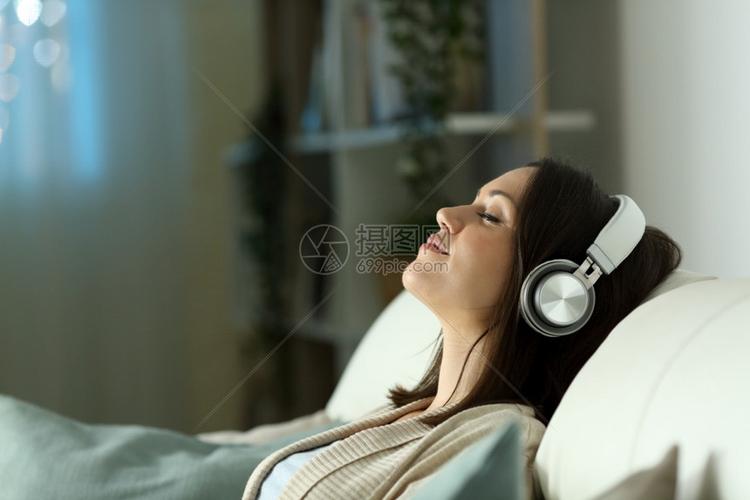 一位放松的女在晚上用耳机听音乐坐在家中客厅的沙发上
