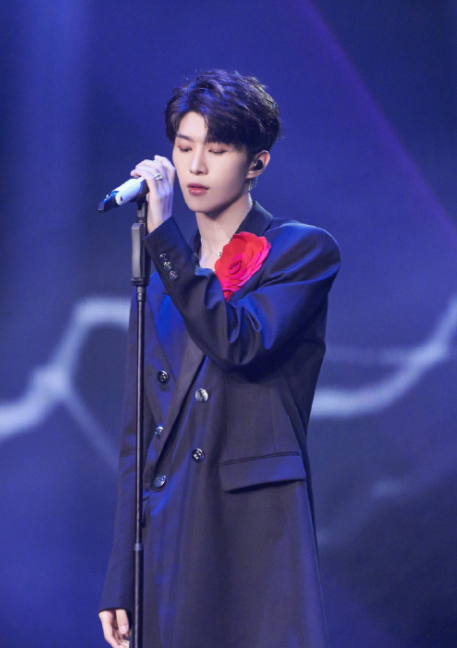 范丞丞舞台穿搭造型,身穿廓型大衣胸口佩戴红色山茶花