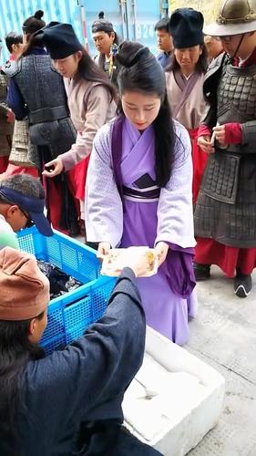 穿着粗衣麻布的美女群演排队中取用午餐,后面那位拿着自己那一