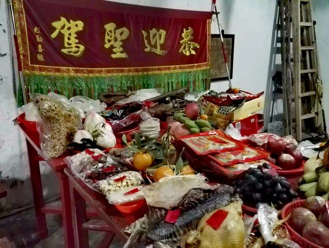 族亲就在村公厅前的八仙桌拼成的案台陆续摆放祭拜神明供品,大多有