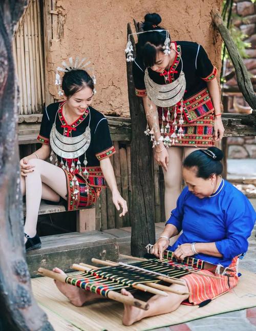 身穿黎族服饰的姑娘们在观看阿婆编织黎锦