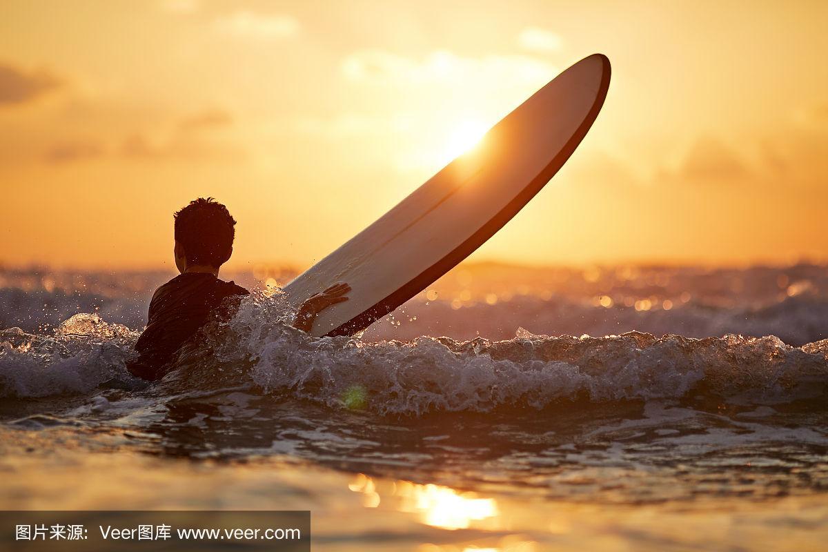 夕阳下,自信的男孩背着冲浪板站在海边