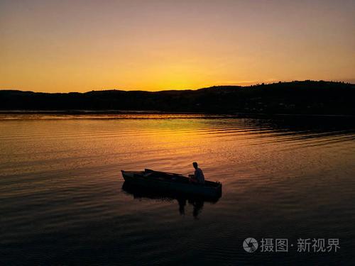 孤独的家伙坐在小船在日落