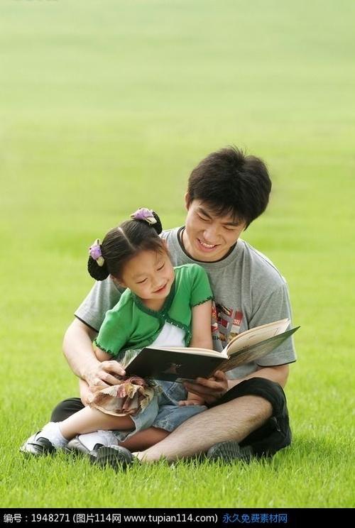 男人抱着小女孩看书坐在草地上看书