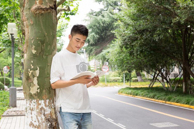 拿着书站在校园树下看书的男生