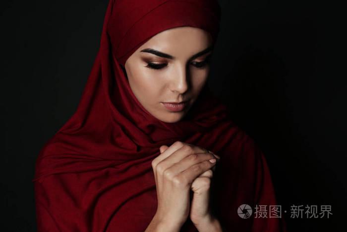 穆斯林妇女戴头巾在黑暗背景下祈祷的肖像