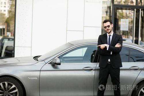 优雅的商人站在外面与折叠的武器, 私人司机等待他的老板指向豪华轿车