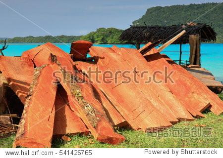 heap of reddish wood battens piled together beside a thatch