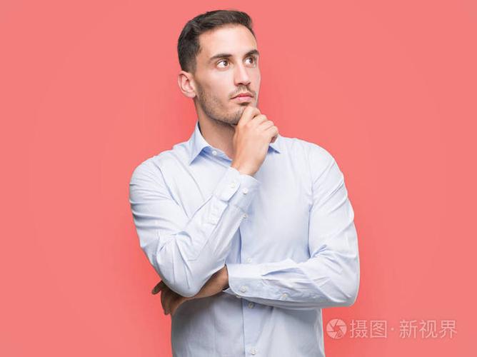 英俊的年轻商人看着自信的相机与交叉的手臂和手举起下巴.积极思考