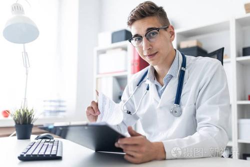 年轻医生拿着剪贴板,坐在办公桌前照片-正版商用图片0