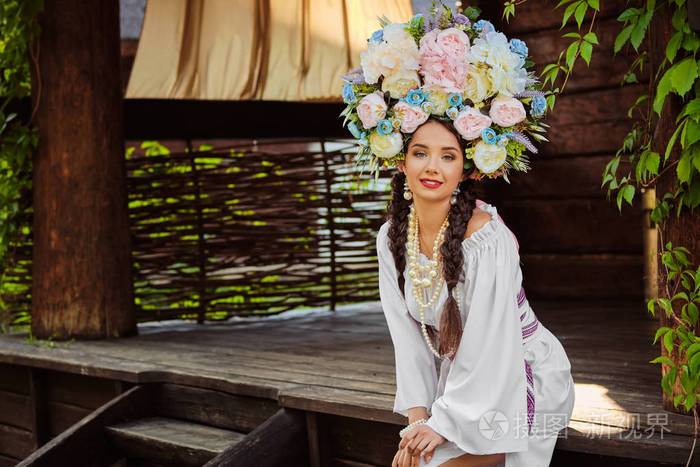 一个黑发女孩穿着白色的乌克兰正宗民族服装,戴着花环,对着一个绿色的