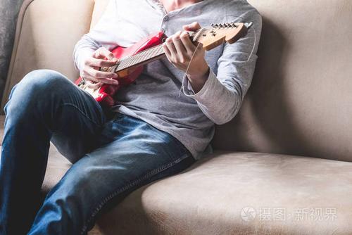 休闲的年轻男子在家里的沙发上弹吉他