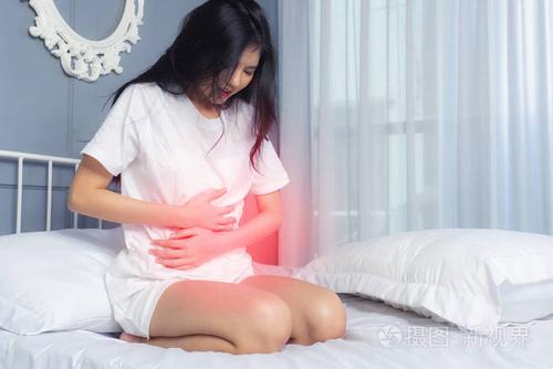 年轻女子在家坐在白色的床上腹痛. 别再睡过头了