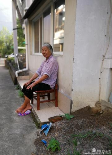 老婆婆一人孤寂地坐在墙边,看人来人往.