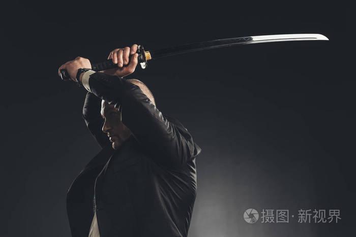 在西装的人的侧面看用武士刀剑在黑色孤立的命中