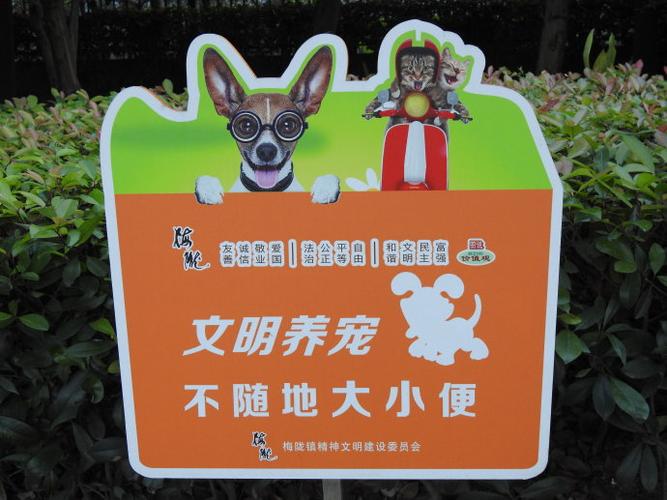 马路边草坪上竖立的有狗,猫头像的"文明养宠,不随地大小便"宣传