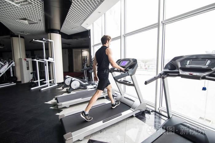 跑得快.侧面图的运动服在健身房的跑步机上的年轻人
