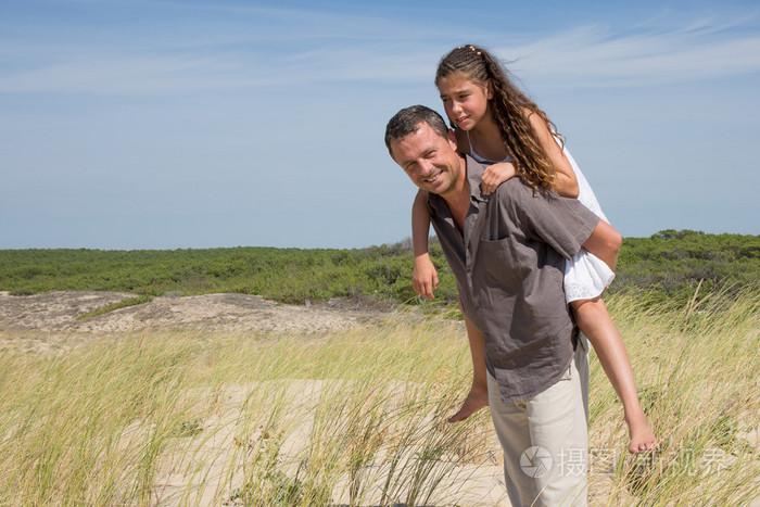 可爱的年轻女孩骑在她爸爸的肩膀上外背驮式