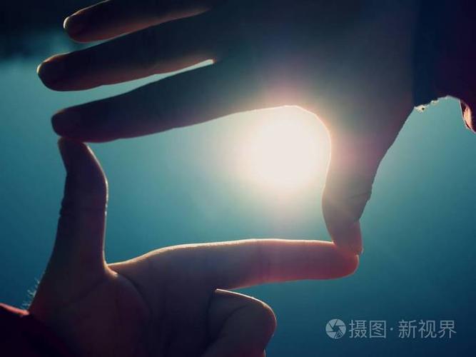 女性手做手指形状的手势,手握太阳耀斑在海滩上.照片