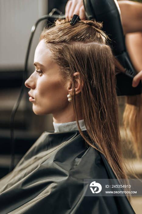 cropped shot of hairstylist drying hair to beautiful young woman