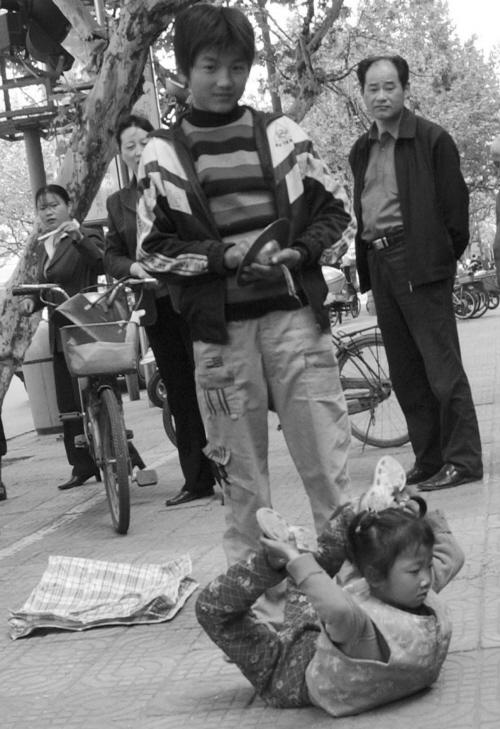有一男一女两个孩子在表演杂技卖艺,其中正在表演的女孩子看上去只有5