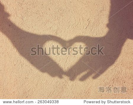 two hands forming a heart shadow on the wall