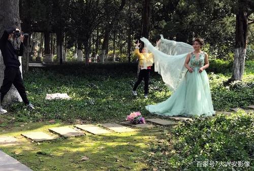 春意盎然的公园里,摄影师正在给美女拍照,一名小女孩当助理,其乐融融.