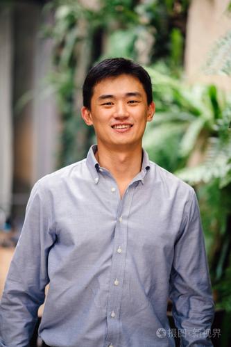 一位英俊,年轻,聪明的中国亚洲男人穿着西装,微笑着站在绿色的墙上.