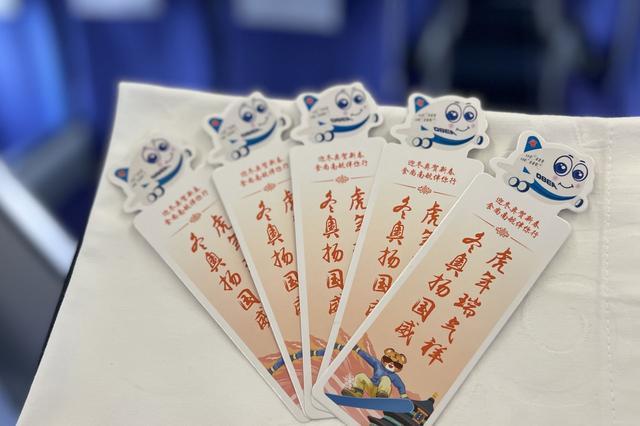 乘务员为正在读书的旅客送上精美的奥运书签,给旅客带来一份冬奥会小