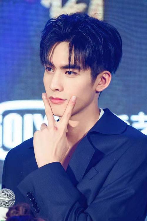 宋威龙穿着一件深色的西装,单手比耶.