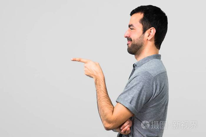英俊的男人手指着侧面在灰色背景上展示一种产品