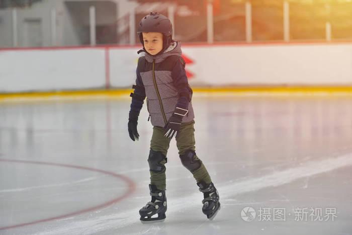 可爱的小男孩穿着冬天的衣服在溜冰场上滑冰